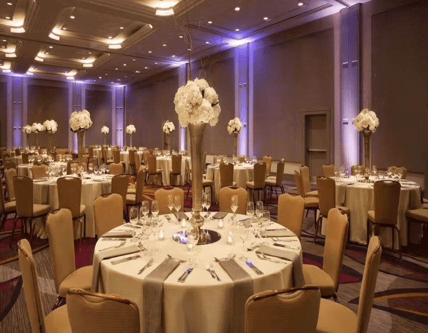 Upscale banquet hall with round dining tables, floral centerpieces, and ambient purple lighting for formal events