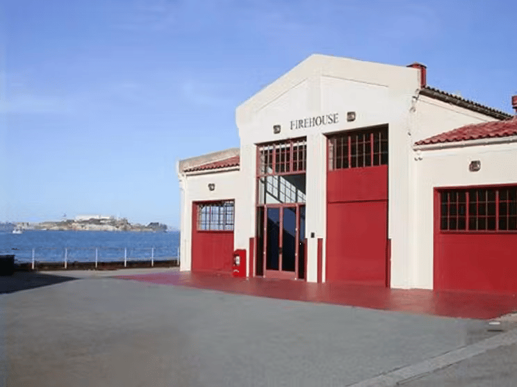 Modern waterfront event venue exterior with red doors, industrial architecture, and coastal surroundings