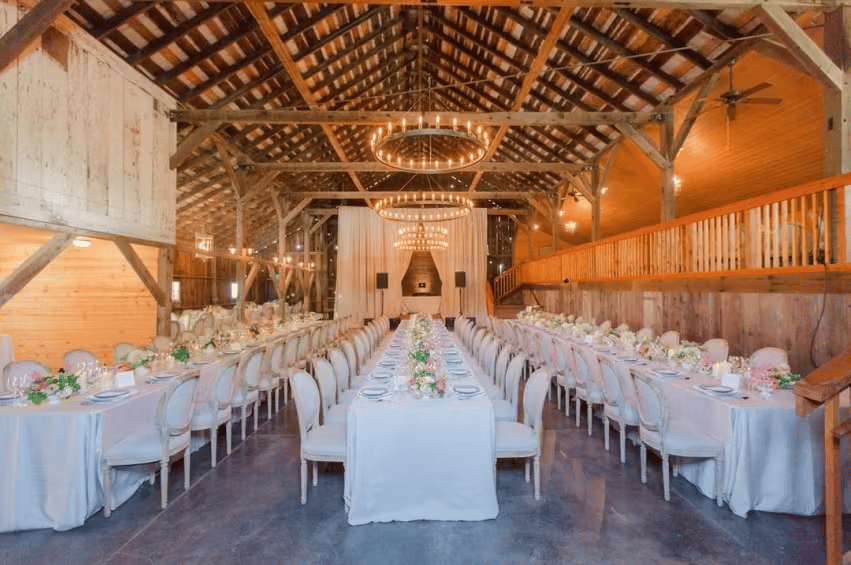 Rustic luxury wedding venue with long banquet tables, vaulted wood ceilings, and warm ambient lighting