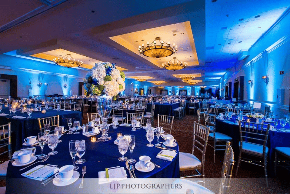 Upscale ballroom reception with blue ambient lighting, floral centerpieces, and elegant event dining setup
