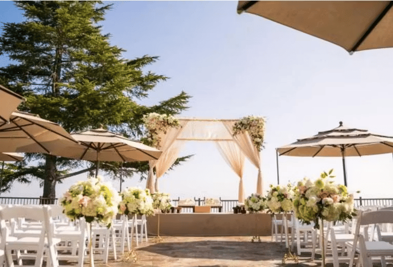 Outdoor beachfront wedding ceremony setup with draped archway and scenic oceanfront views