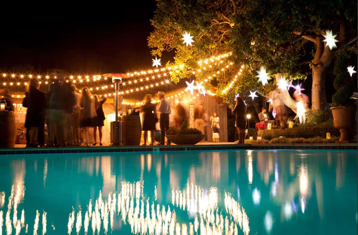 Outdoor evening event space with string lights, poolside ambiance, and elegant social gathering atmosphere