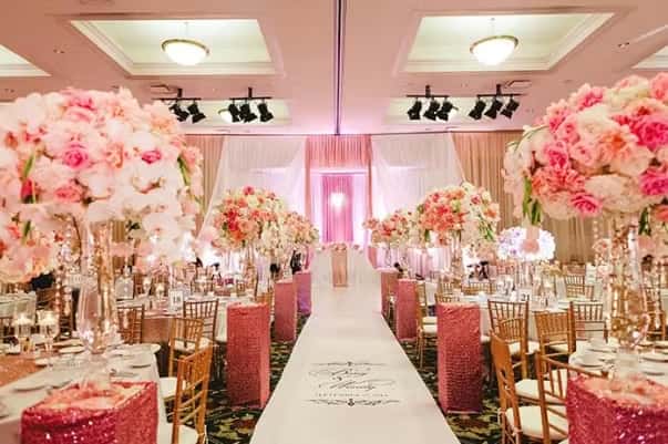 Romantic wedding aisle with pink floral decor, elegant lighting, and luxurious reception styling