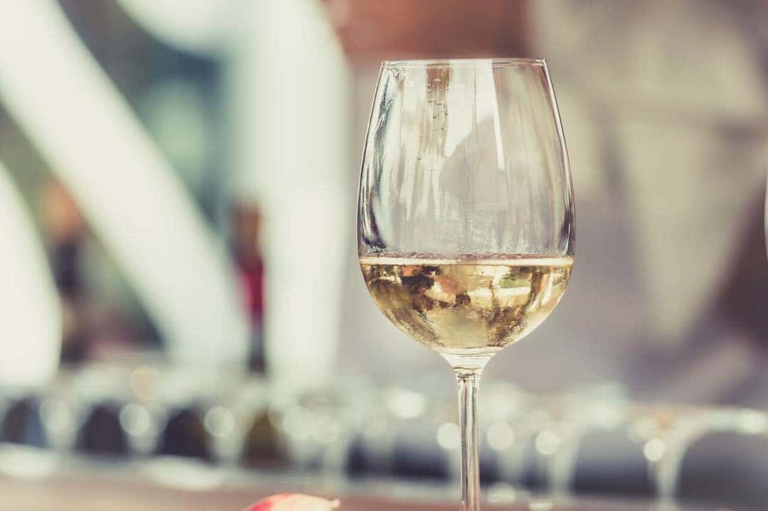 A glass of chilled white wine on a bar counter with blurred bottles and glasses in the background.