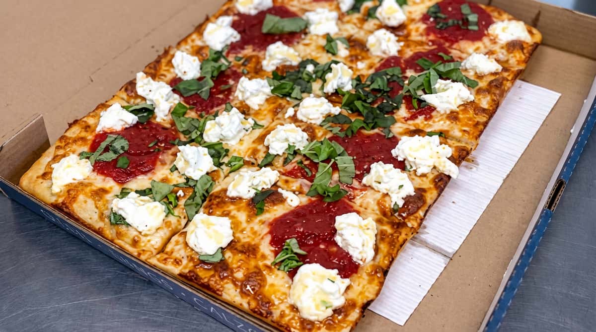 Red sauce pizza topped with dollops of ricotta cheese and fresh basil, cut into squares.