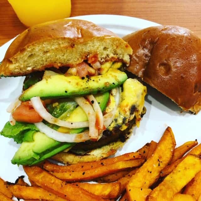sandwich with avocado, onions and tomato on a bun with a side of fries