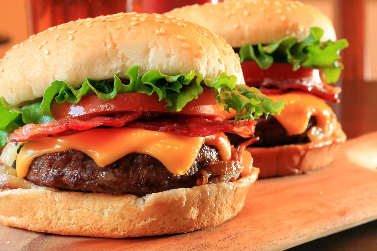 two cheeseburgers topped with bacon, lettuce and tomato