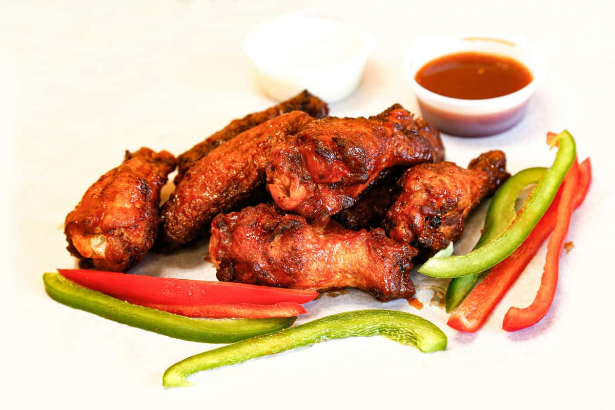 Crispy buffalo chicken wings with red and green bell pepper slices and dipping sauces—bold, flavorful bar food appetizer.