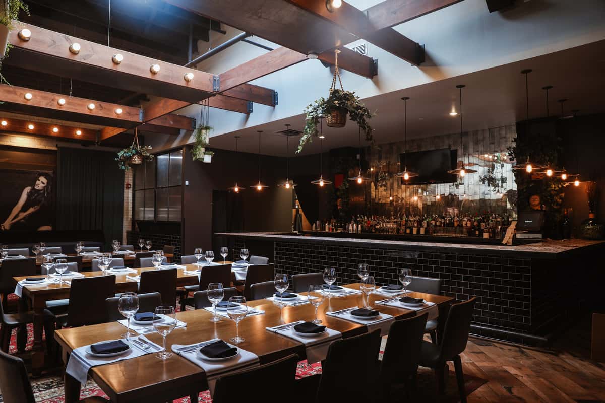 Dark ambient romantic dining venue with flexible seating options for both large and intimate groups, characterized by the rich allure of dark wood beams and accents.