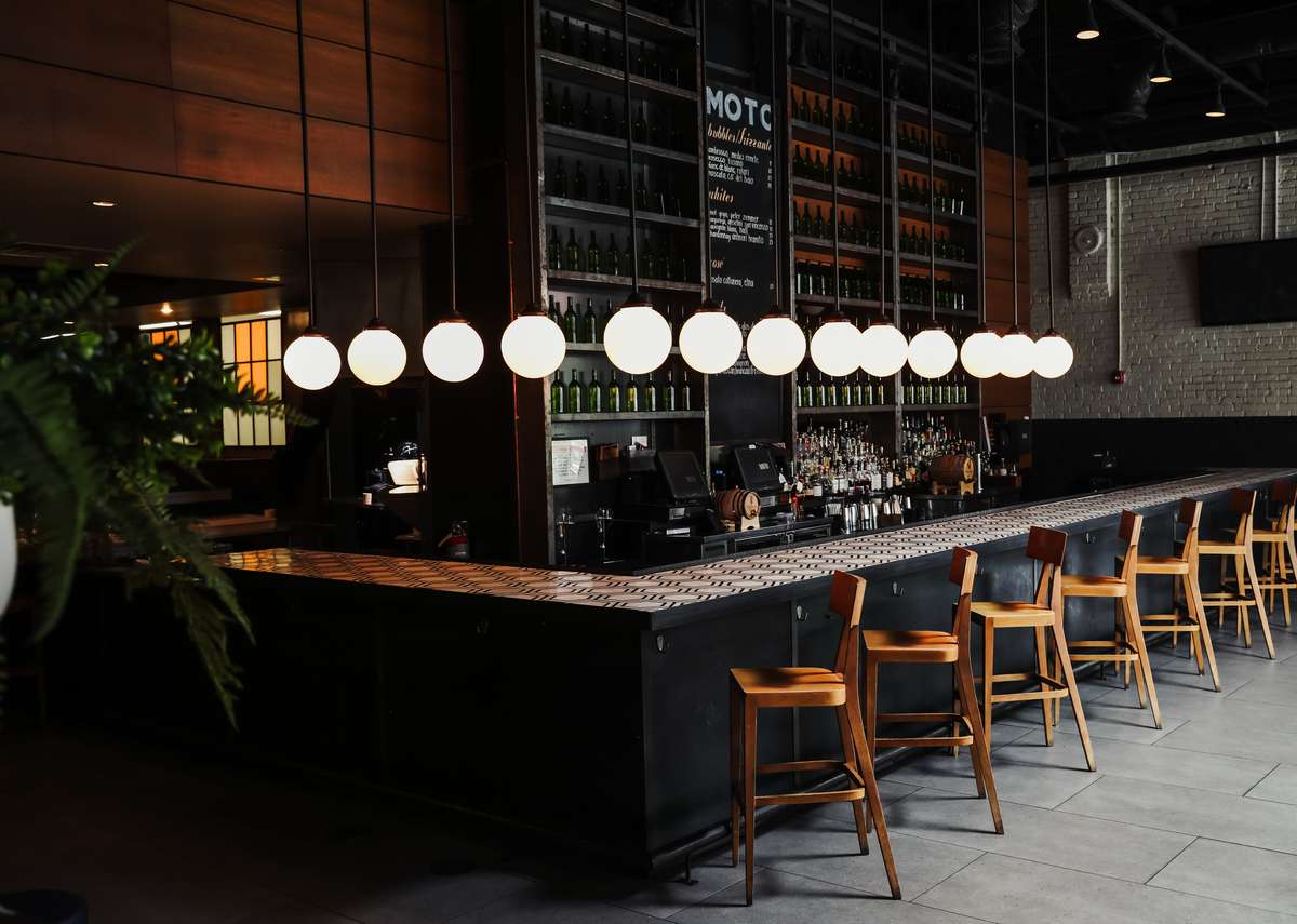 Stylish bar setup featuring light wood bar stools, a dark base, marble countertops, and elegant circle pendant lighting.