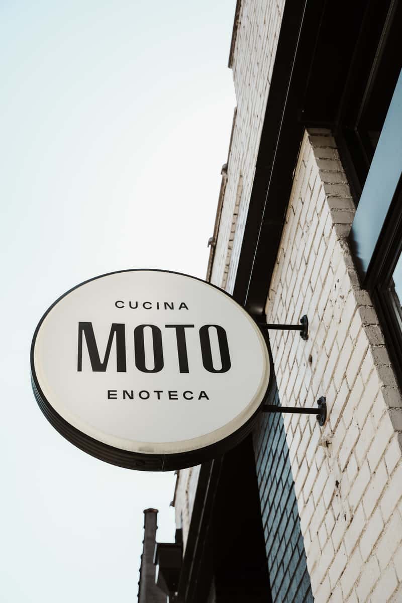 Exterior circular sign of MOTO connected to white washed brick