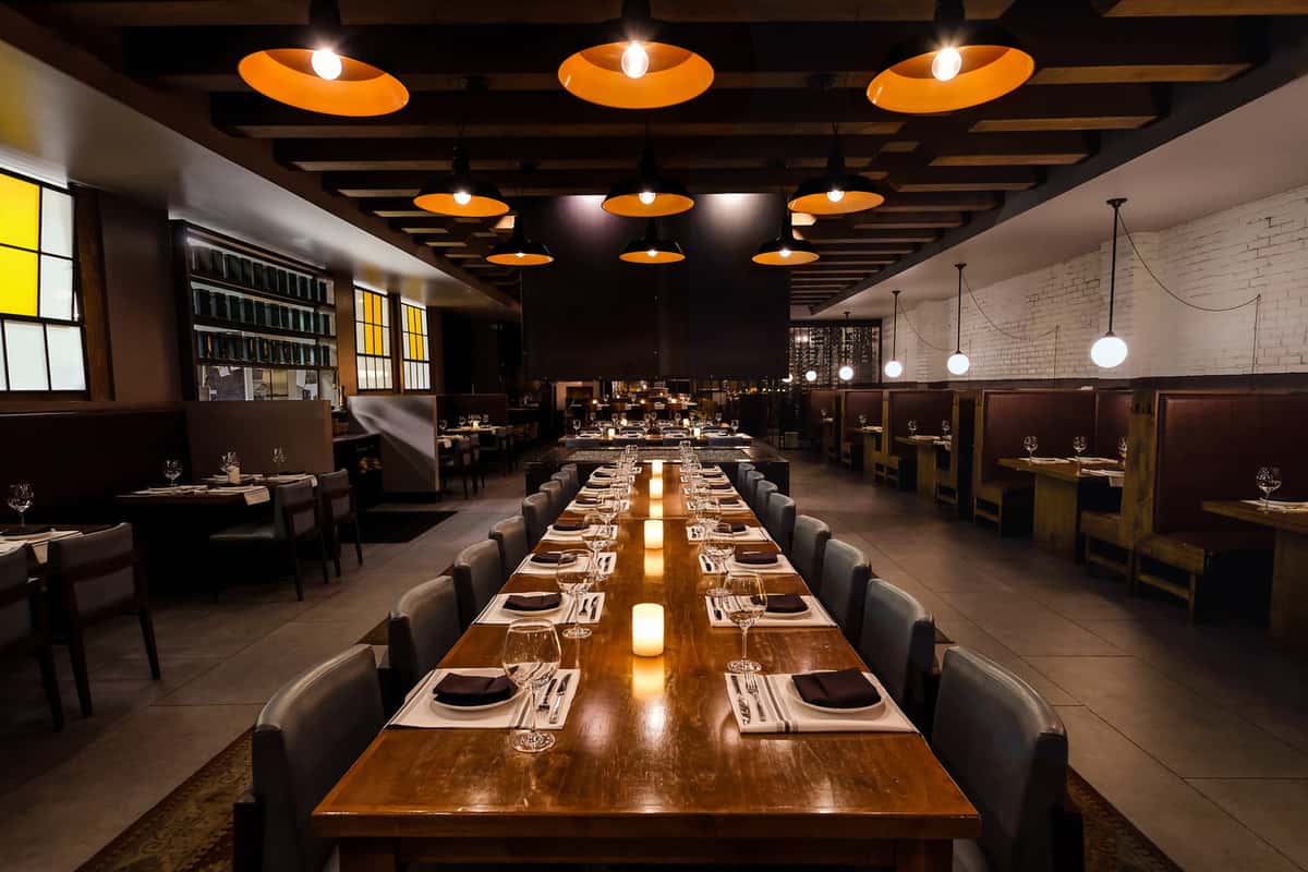 Spacious dining room with white washed brick walls and dark wood accents with sparkling pendant lighting.