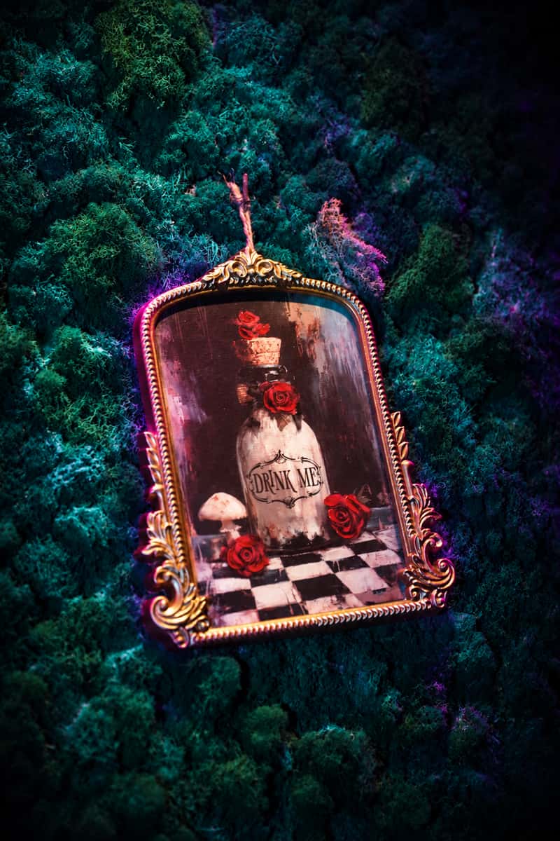 Ornate gold Drink Me picture frame on a moss wall with violet highlights