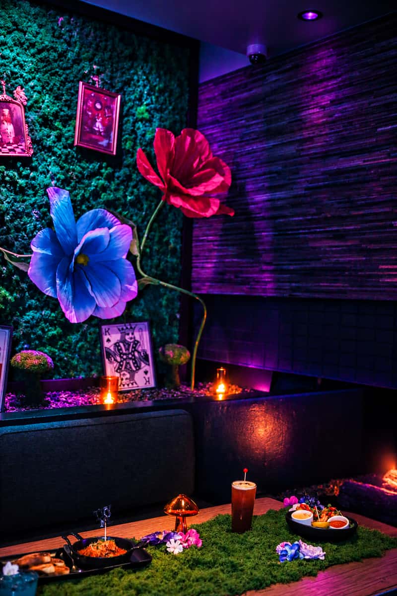 Mesa dining table with oversized flowers and playing-card decor, treated with teal and violet lighting