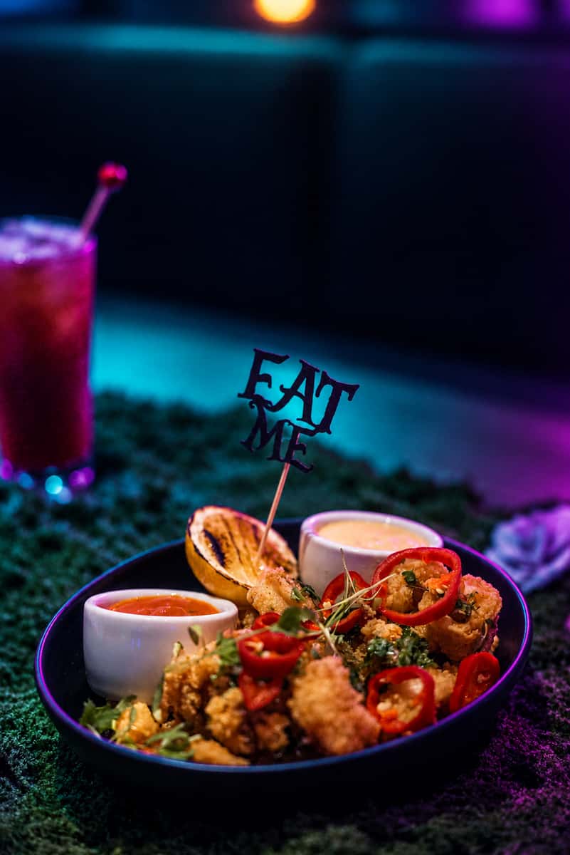 Mesa appetizer with an Eat Me sign, styled with teal and violet lighting