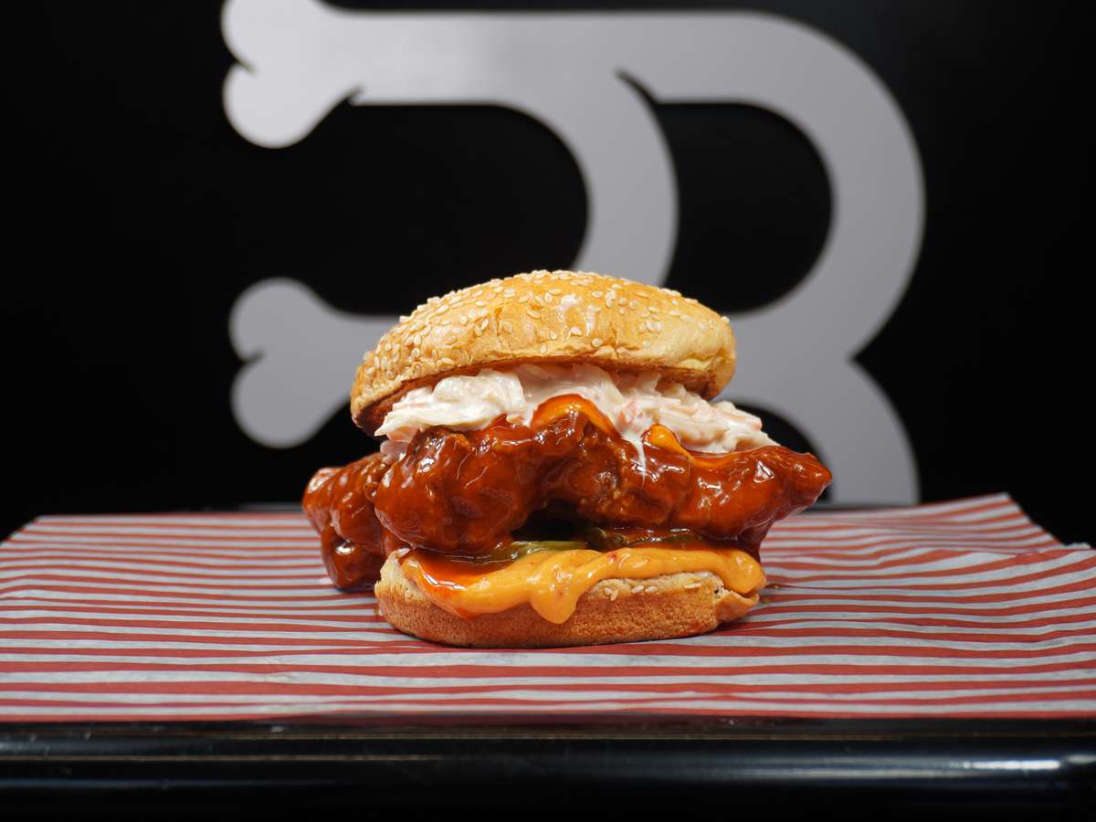 Crispy chicken sandwich with spicy glazed tenders, melted cheese, pickles, and creamy slaw on a sesame bun