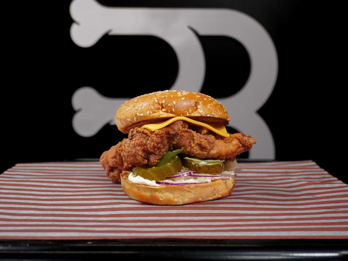 Crispy chicken burger with fried fillet, cheese, pickles, and slaw on a sesame seed bun