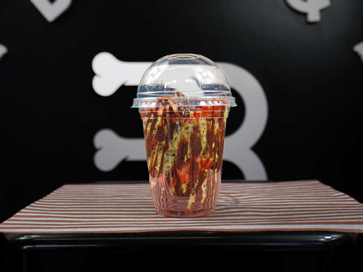 Dessert cup layered with strawberries, chocolate drizzle, and creamy filling in a clear takeaway cup with dome lid