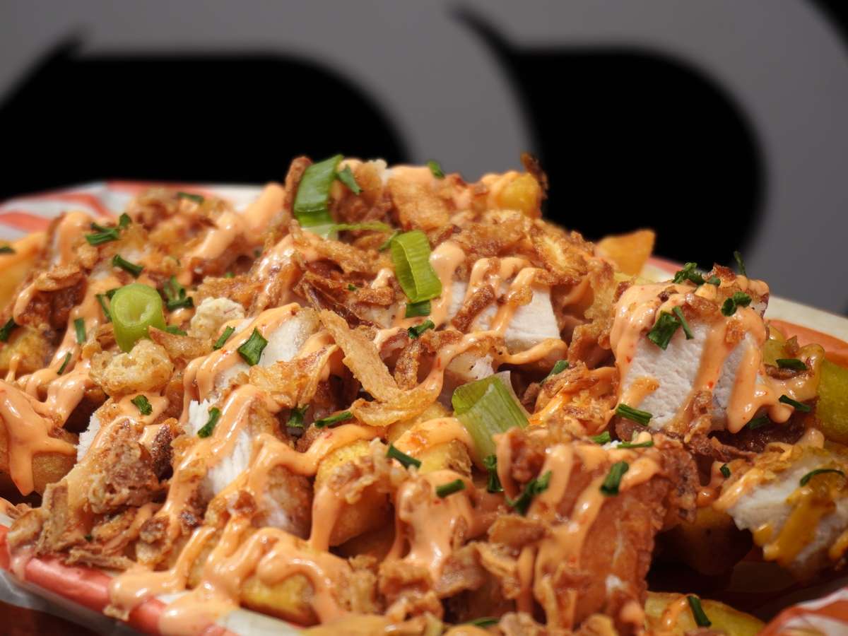 Loaded fries topped with crispy chicken pieces, melted cheese, creamy sauce, and garnished with green onions and crispy onions