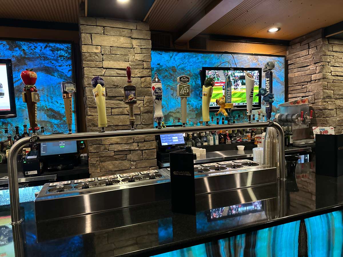 A well-stocked bar, possibly within a restaurant, features multiple beers on tap. Stone accents and a television playing sports complete the inviting atmosphere.