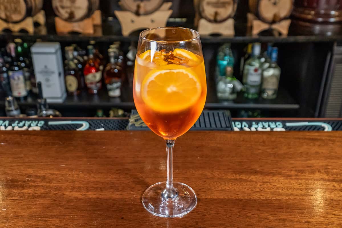 Aperol Spritz with an orange wheel in a wine glass on a wooden bar
