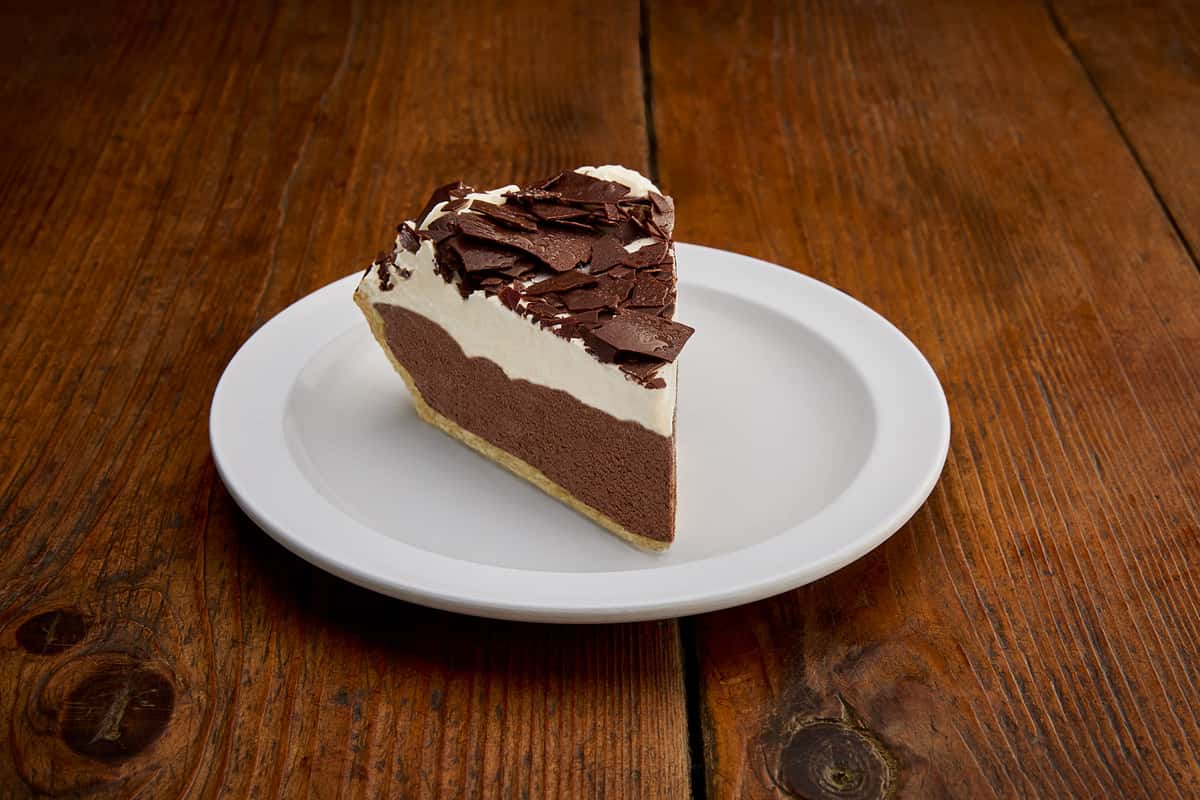 A decadent slice of chocolate cream pie featuring a rich, velvety chocolate filling nestled in a flaky pie crust. Topped with whipped cream and chocolate shavings, this indulgent dessert offers a perfect balance of creamy texture and deep chocolate flavor, making it a sweet ending to any meal.