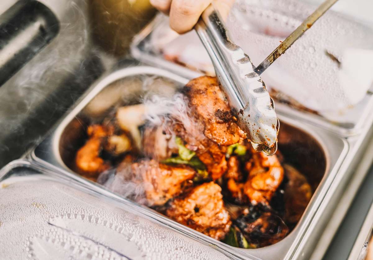 Close-up of steaming hot grilled chicken being served with tongs from a catering tray