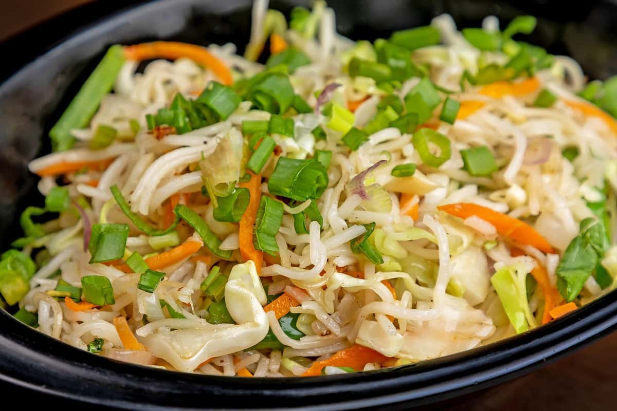 Stir-fried hakka noodles with cabbage, carrots, spring onions, and green bell peppers served in a black bowl.