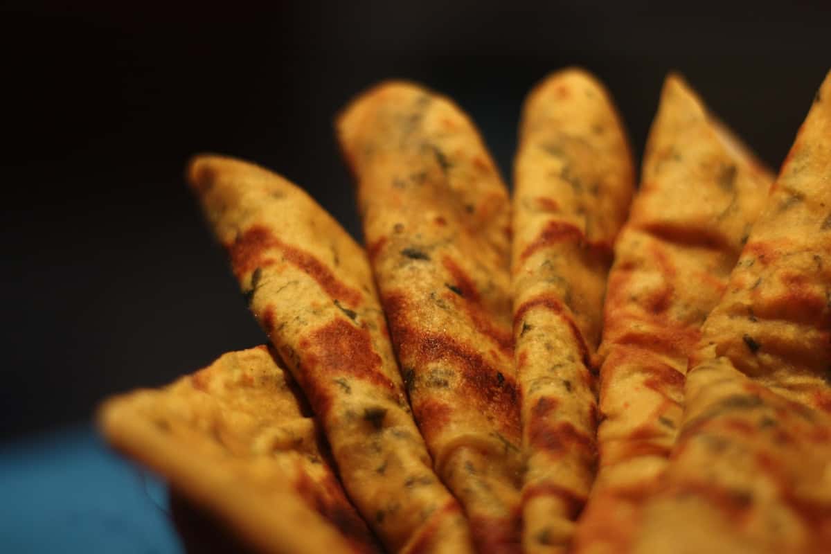 Close-up of freshly cooked methi theplas stacked in a basket, showcasing their golden-brown texture and herb-infused surface.
