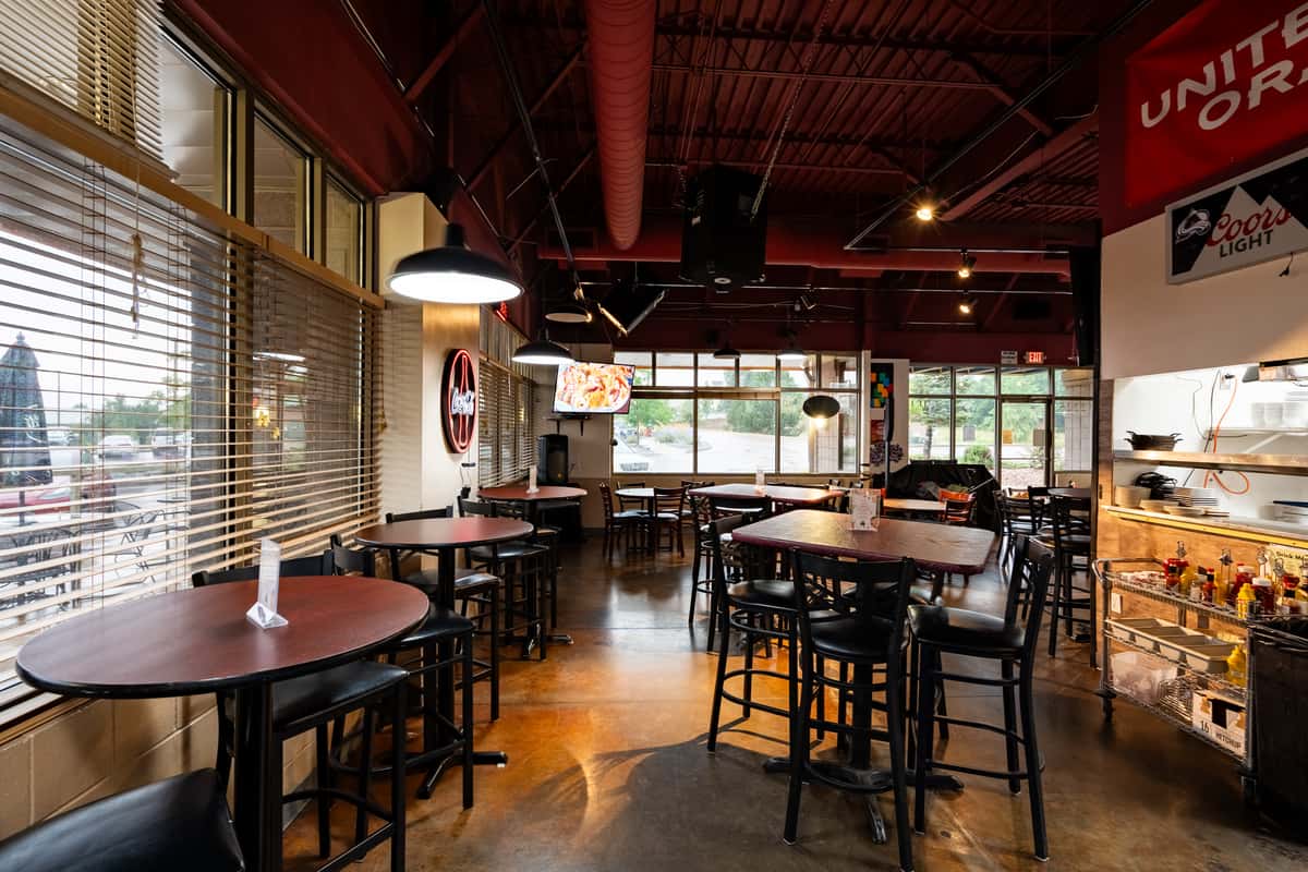 Spacious dining area at Parkway Tavern featuring high-top tables, large windows with blinds, warm ambient lighting, and sports-themed décor, creating a relaxed and inviting atmosphere.