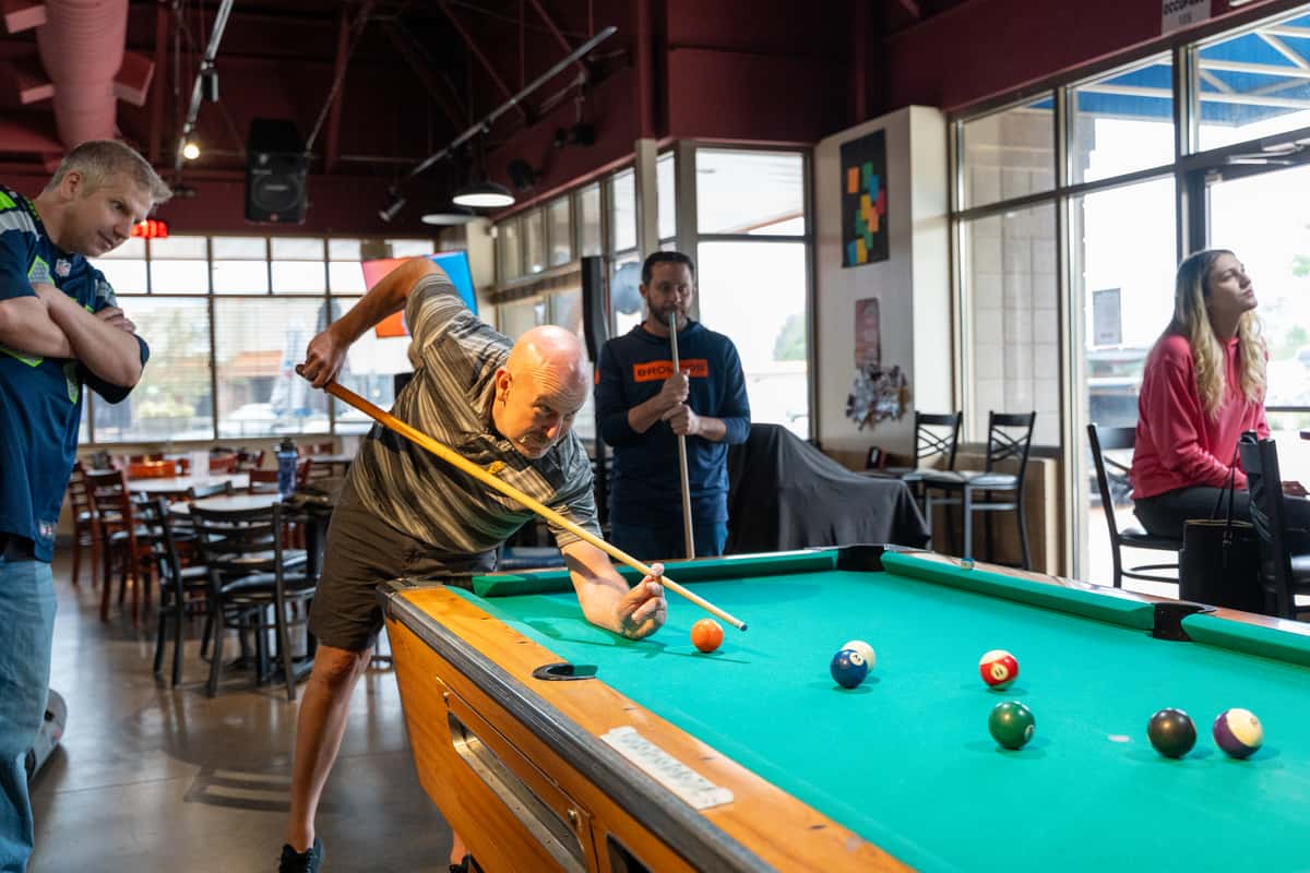 Guests enjoying drinks and casual conversation while a man takes a shot at the pool table inside Parkway Tavern, a lively neighborhood bar and grill with a relaxed social atmosphere.