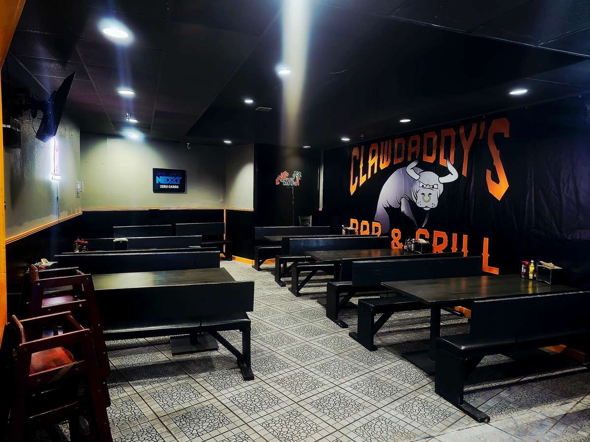 Restaurant seating area with dark benches and a large Clawdaddy's Bar & Grill mural on the wall.