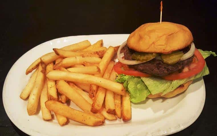 Cheeseburger on brioche bun with lettuce, tomato and onion with side of French fries.