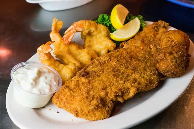 fried fish on a plate with fried shrimp, tartar sauce and lemon wedges.