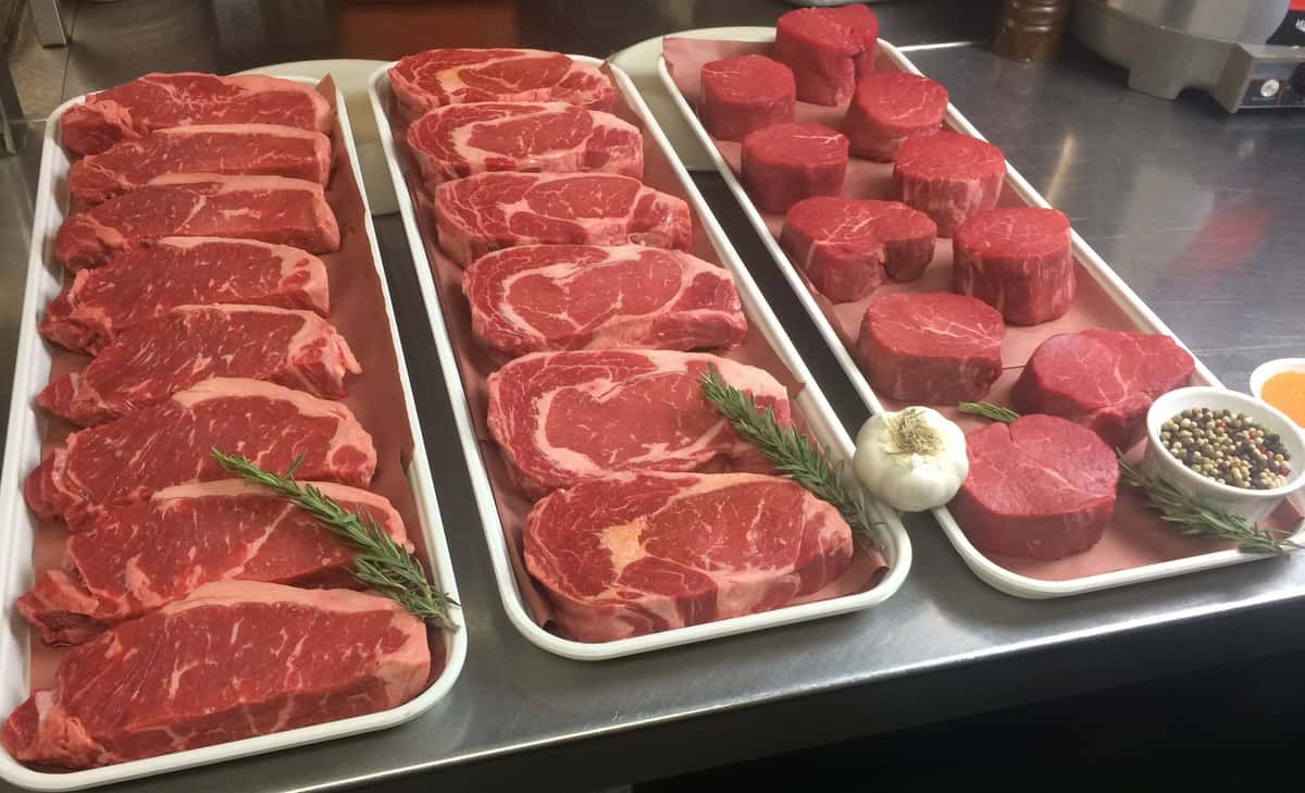 three trays of raw meat cuts with rosemary and garlic