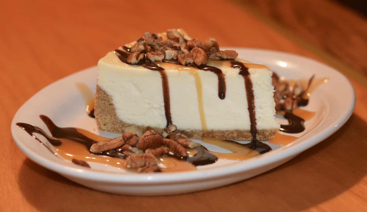 piece of cheesecake topped with nuts and drizzled chocolate syrup and caramel