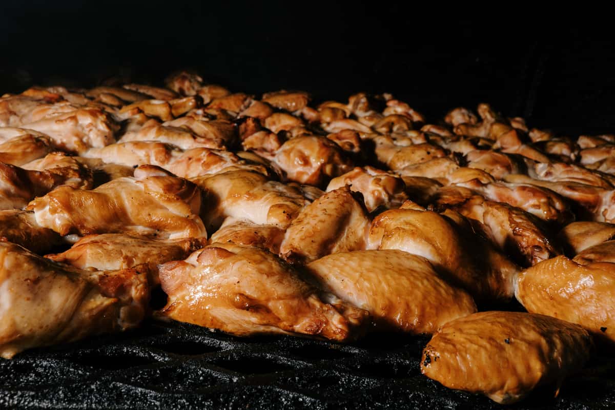 A close-up view of multiple pieces of chicken wings grilling on a barbecue, with the skin browning and caramelizing.