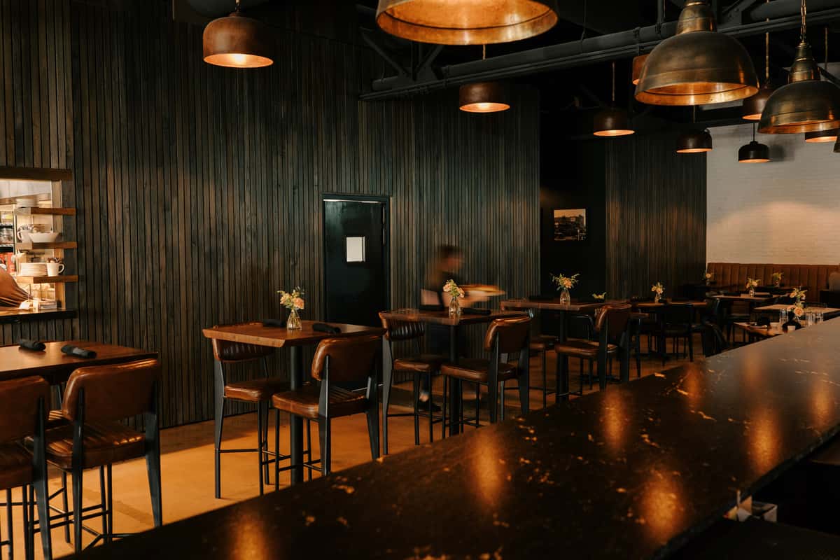 Chic steakhouse interior with dark wood paneling, leather seating, warm pendant lighting, and small floral arrangements on each table.