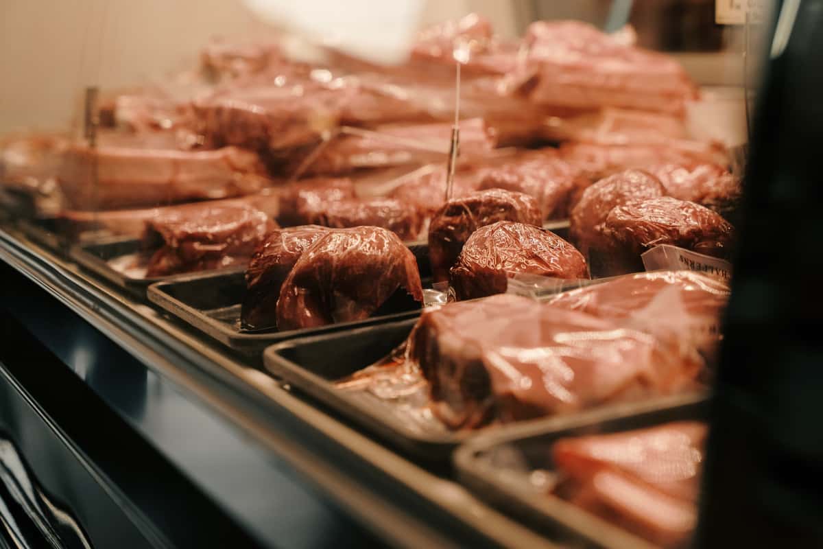 A display of various cuts of meat wrapped in plastic, neatly arranged on trays in a refrigerated case.