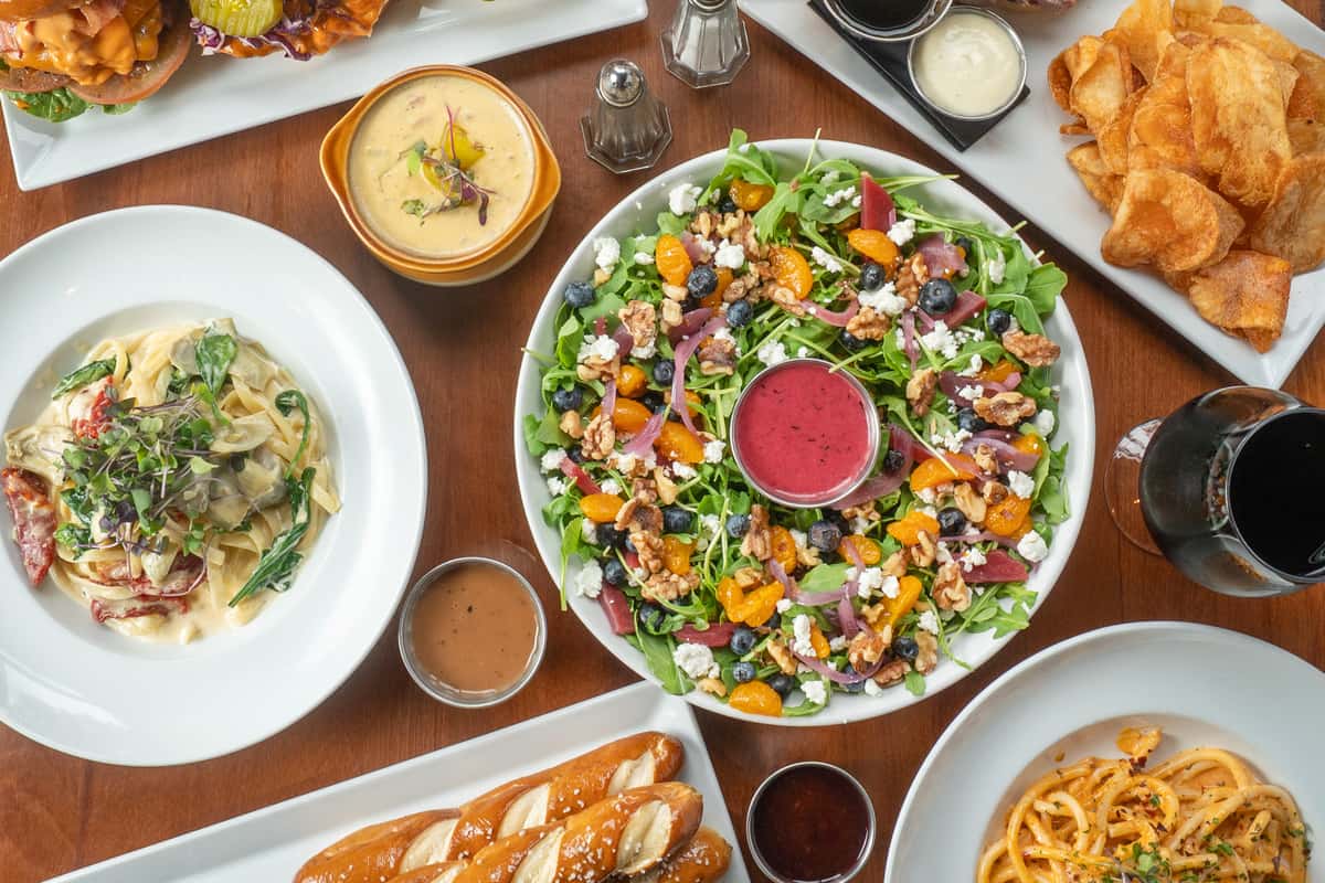 A plate of salad surrounded by drinks, appetizers and entrees on a table