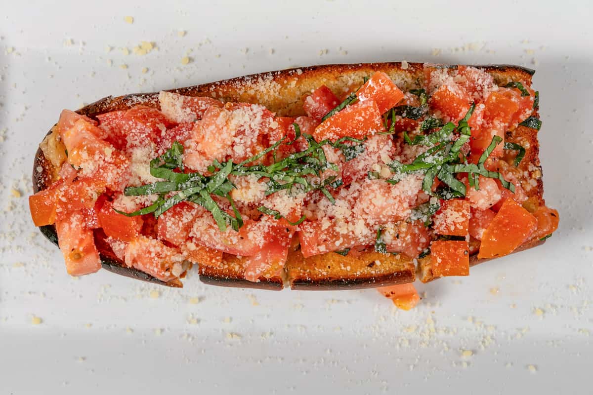 Toasted Italian bruschetta topped with fresh diced tomatoes, grated Parmesan cheese, and chopped basil on a white plate.