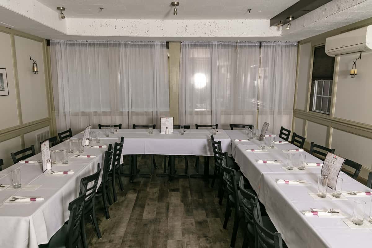 Private dining room with U-shaped table arrangement, white tablecloths, black chairs, and soft lighting—ideal for events, parties, or group reservations.