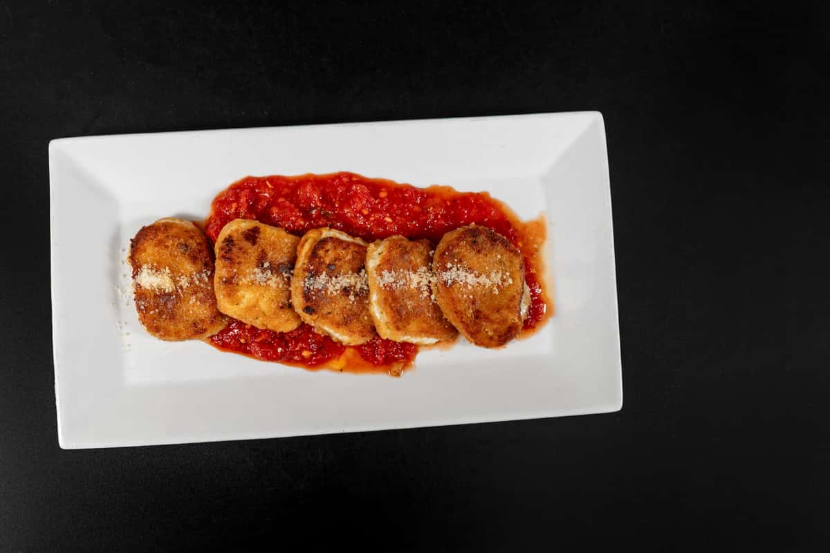 Golden-fried ravioli served over a bed of marinara sauce and topped with grated Parmesan on a rectangular white plate.