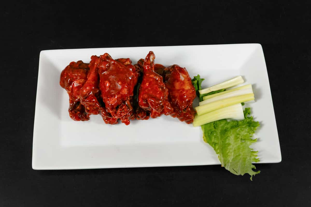 Spicy buffalo chicken wings coated in tangy red sauce, served with celery sticks and romaine lettuce on a rectangular white plate.