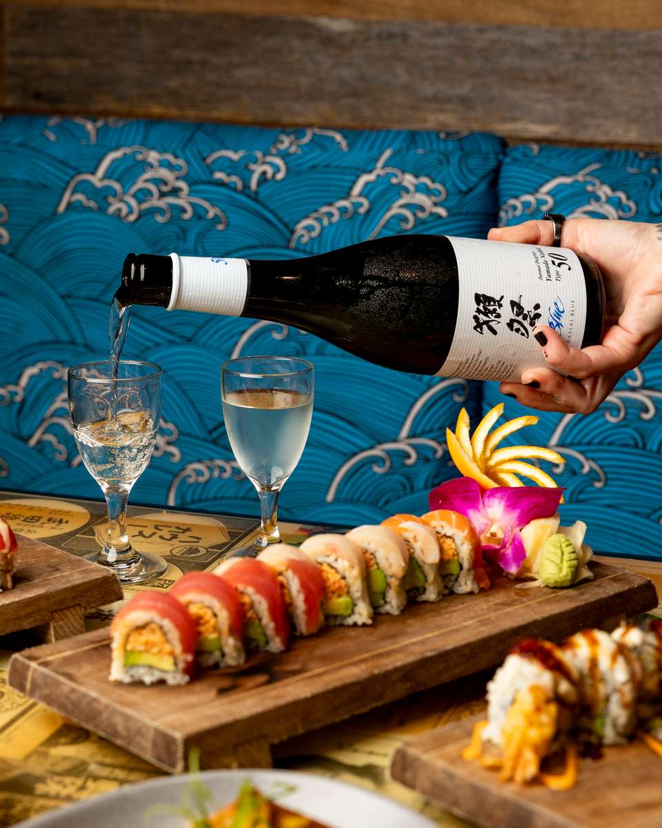 Premium sake being poured alongside a fresh specialty sushi roll at Kapow! Noodle Bar, pairing elevated Japanese beverages with modern Asian fusion dining.