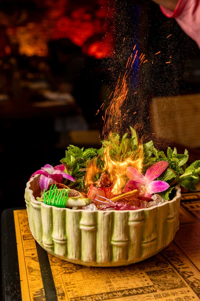 Flaming seafood presentation with shrimp, fresh greens, and edible flowers served in a bamboo-style bowl at Atlantic Current restaurant