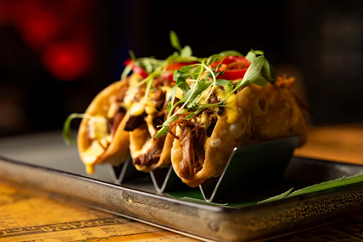 Asian fusion street-style tacos topped with fresh slaw, herbs, and bold flavors at Kapow! Noodle Bar, perfect for sharing during happy hour or late-night dining.