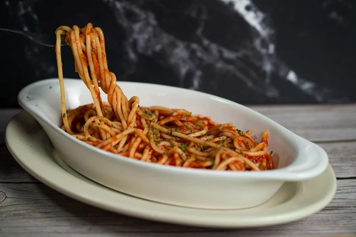 Spaghetti tossed in marinara sauce, served in a white dish with herbs sprinkled on top and a fork twirling noodles.