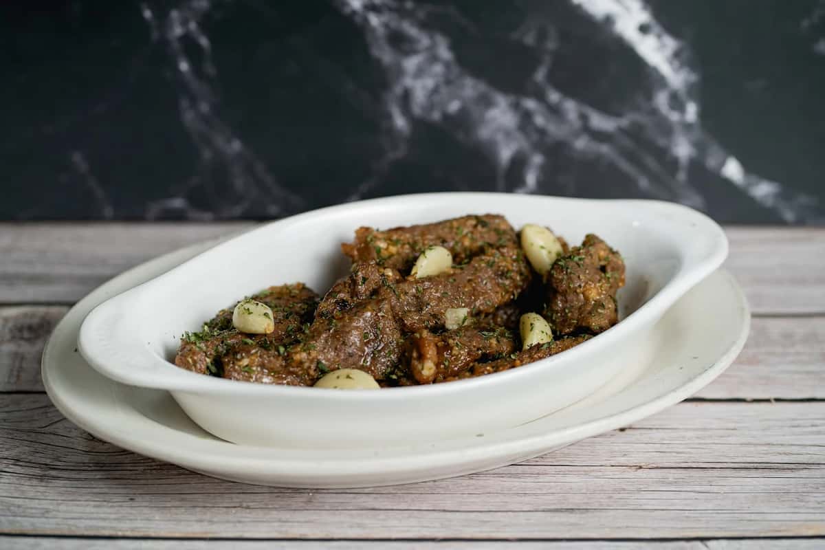 Seasoned Italian sausage pieces garnished with garlic cloves and herbs, served in a white oval dish.