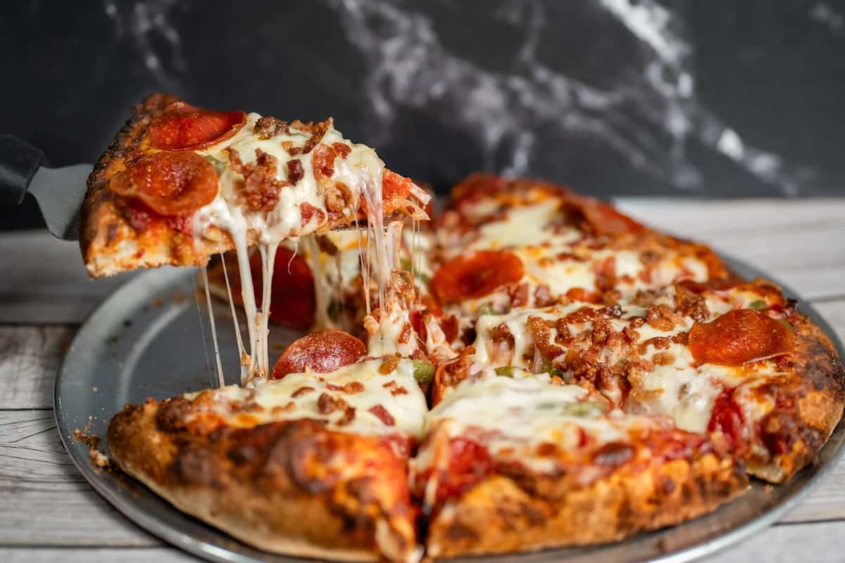 A cheesy slice of pepperoni and sausage pizza being lifted from a pan, with gooey melted cheese stretching from the pie.